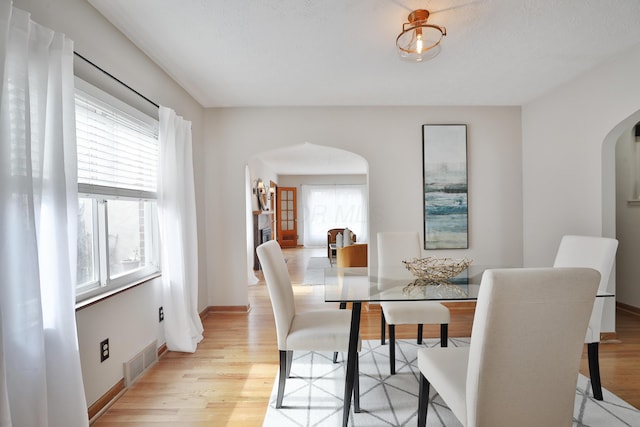 dining space with light wood finished floors, visible vents, arched walkways, and baseboards