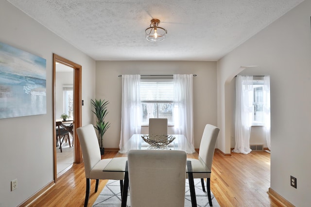 dining area featuring arched walkways, visible vents, light wood-style floors, a textured ceiling, and baseboards