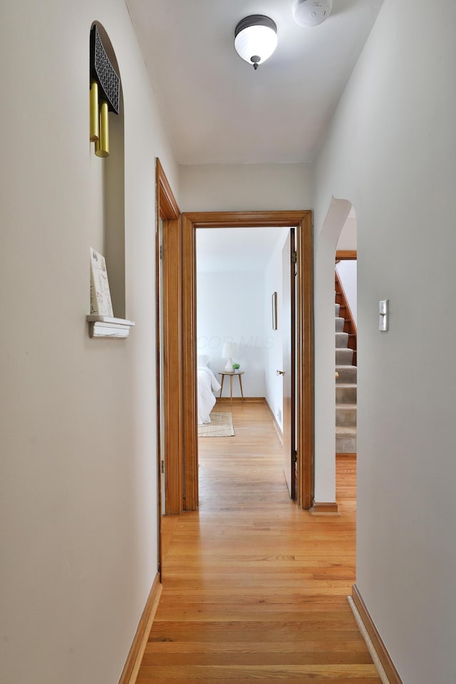 hallway with stairs, light wood-type flooring, arched walkways, and baseboards