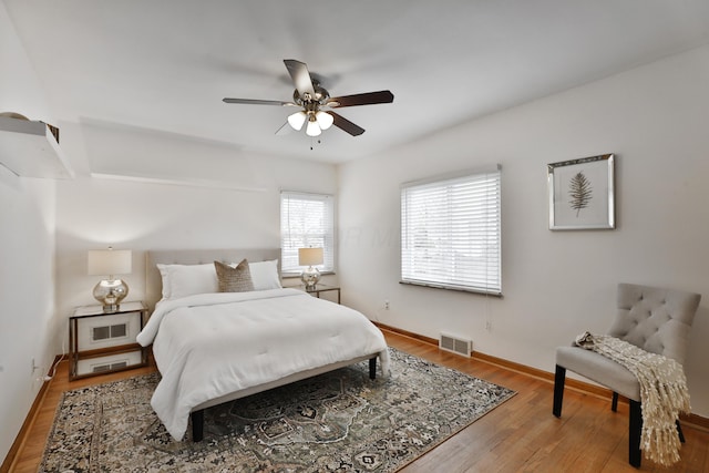 bedroom with a ceiling fan, wood finished floors, visible vents, and baseboards