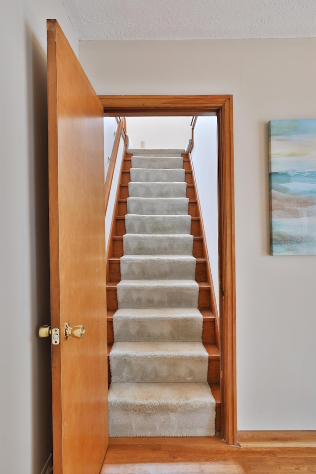 stairway with a textured ceiling and wood finished floors