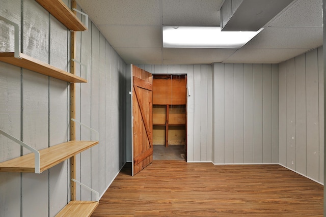 finished basement with wooden walls, a drop ceiling, and wood finished floors