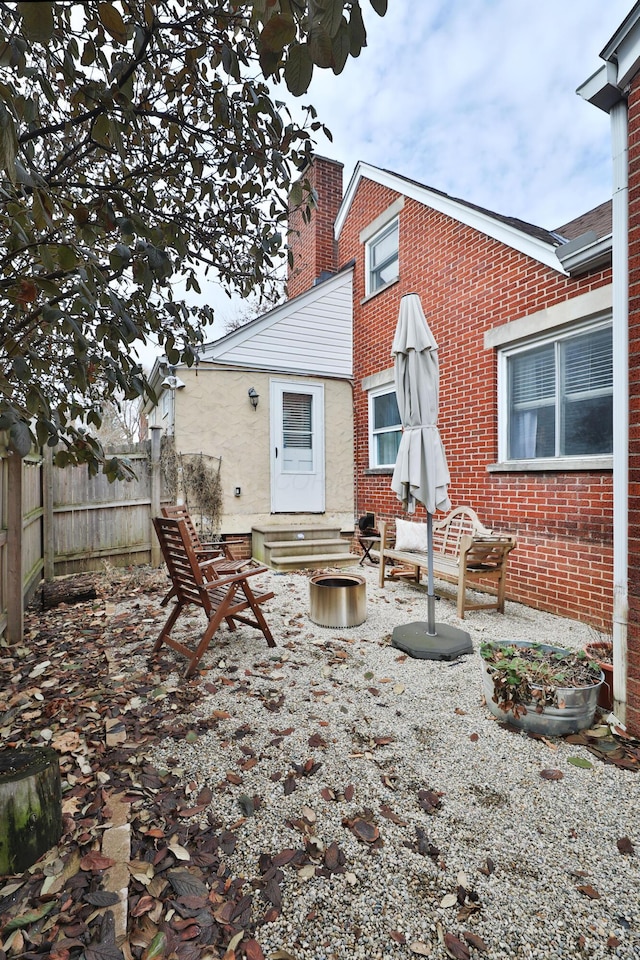 back of house with entry steps, brick siding, fence, and a chimney