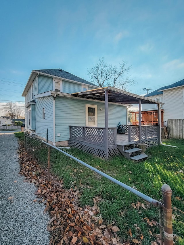 rear view of house with a deck, a lawn, and fence