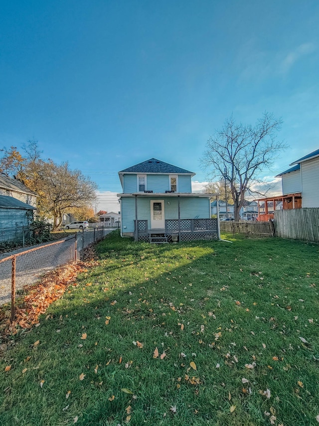 rear view of house with entry steps, a lawn, and fence