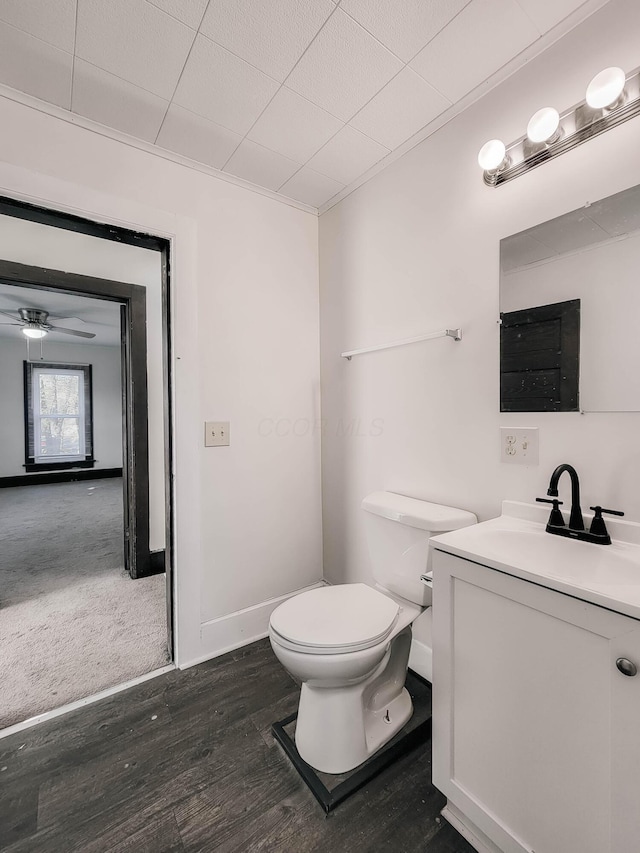 bathroom with toilet, wood finished floors, a ceiling fan, vanity, and baseboards