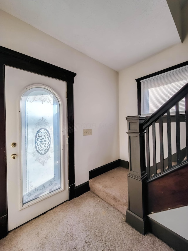 carpeted foyer featuring baseboards and stairway