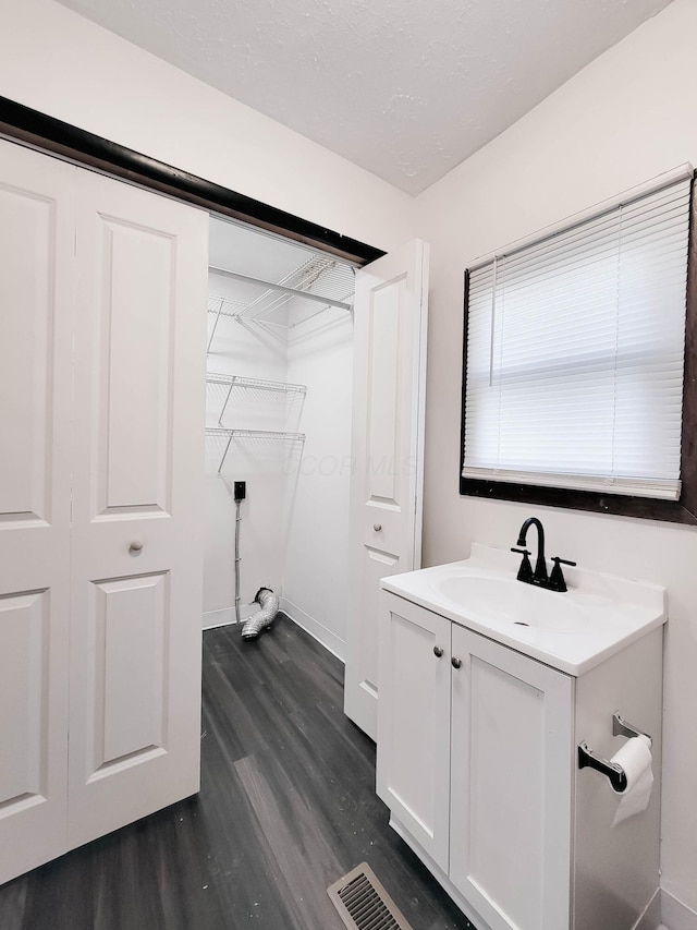 bathroom with a textured ceiling, vanity, wood finished floors, and visible vents