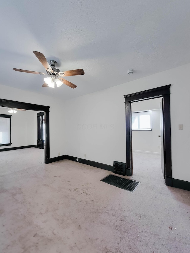 spare room with light carpet, ceiling fan, a textured ceiling, and baseboards