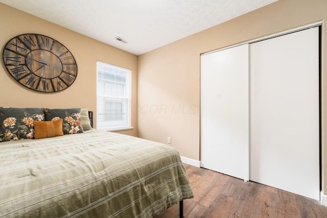 bedroom with a textured ceiling, a closet, wood finished floors, and visible vents