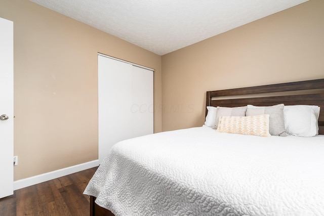 bedroom with a closet, a textured ceiling, baseboards, and wood finished floors