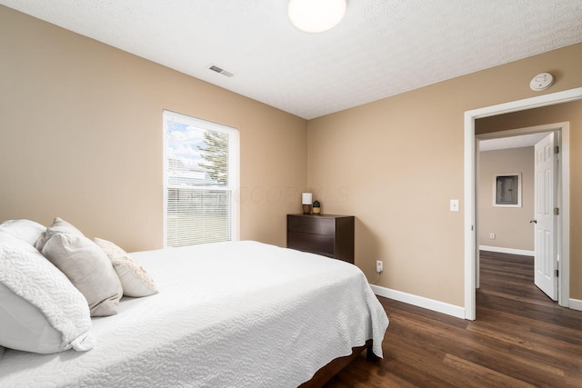 bedroom featuring a textured ceiling, wood finished floors, visible vents, and baseboards