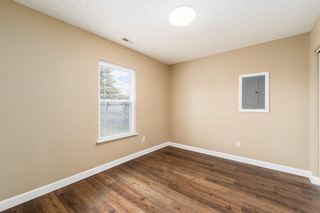 unfurnished room with visible vents, dark wood-style flooring, electric panel, and baseboards