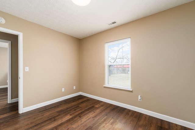 empty room featuring a textured ceiling, dark wood finished floors, visible vents, and baseboards