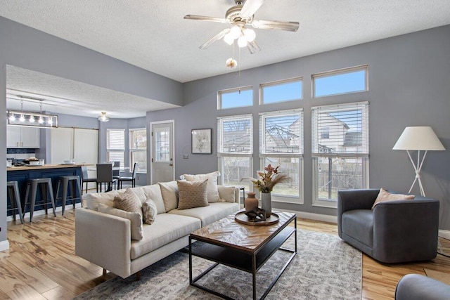 living area with a textured ceiling, ceiling fan, light wood finished floors, and baseboards