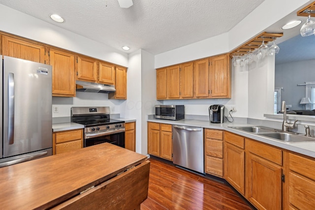 kitchen with dark wood-style flooring, stainless steel appliances, light countertops, a sink, and under cabinet range hood