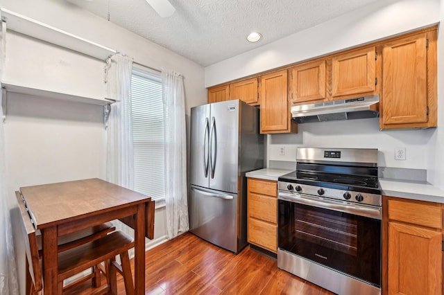 kitchen with appliances with stainless steel finishes, dark wood-type flooring, light countertops, a textured ceiling, and under cabinet range hood