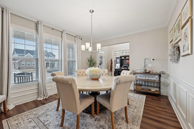 dining space with a decorative wall, crown molding, dark wood-style flooring, wainscoting, and an inviting chandelier