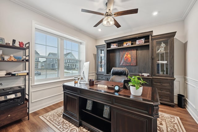 home office featuring a decorative wall, a wainscoted wall, wood finished floors, a ceiling fan, and crown molding