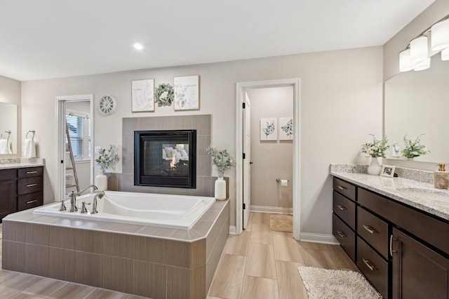 full bath featuring a fireplace, a sink, two vanities, baseboards, and a bath