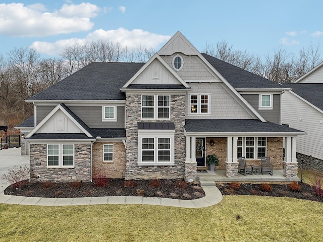 craftsman-style home with covered porch, roof with shingles, a front yard, and board and batten siding