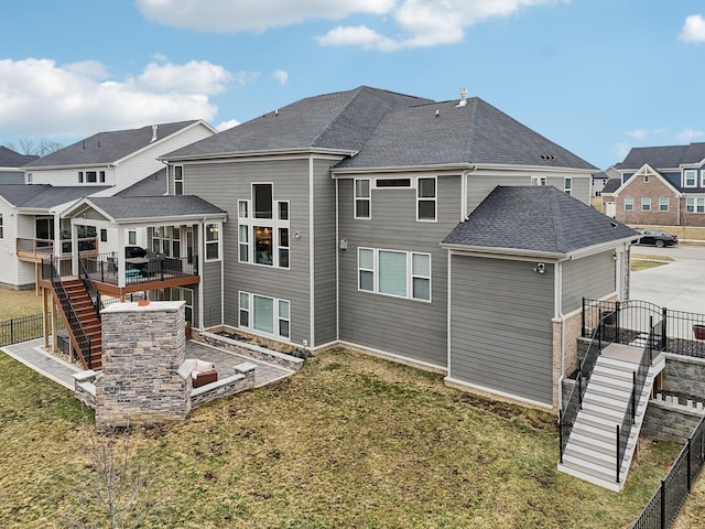 rear view of property with a shingled roof, fence, stairway, and a lawn