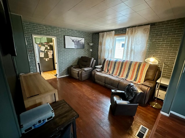 living area featuring brick wall, wood finished floors, and visible vents