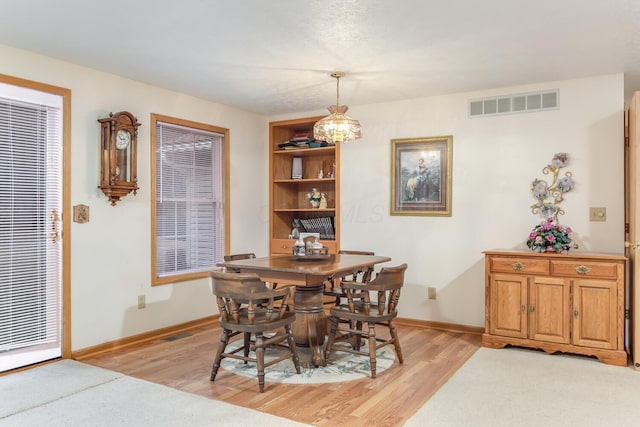 dining space featuring light wood-style floors, visible vents, a notable chandelier, and baseboards