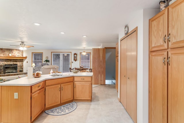 kitchen featuring ceiling fan, open floor plan, light countertops, a stone fireplace, and a sink