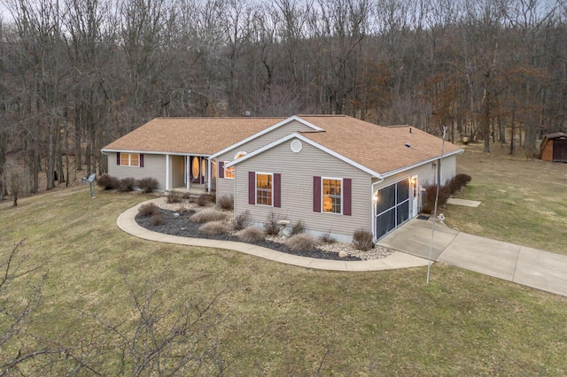 ranch-style home featuring concrete driveway, a front lawn, and a view of trees