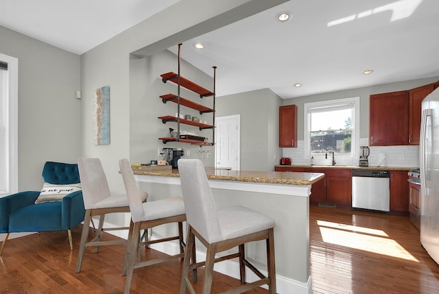 kitchen with a peninsula, appliances with stainless steel finishes, dark wood-style flooring, and a sink