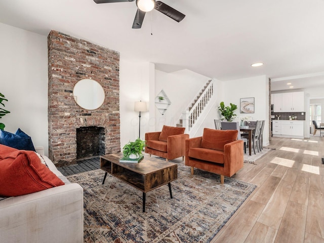 living room featuring light wood finished floors, a ceiling fan, stairs, a fireplace, and recessed lighting