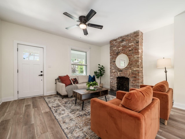 living room featuring light wood-style floors, ceiling fan, a fireplace, and baseboards