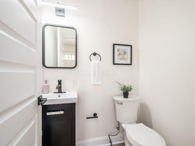 half bath with baseboards, vanity, and toilet