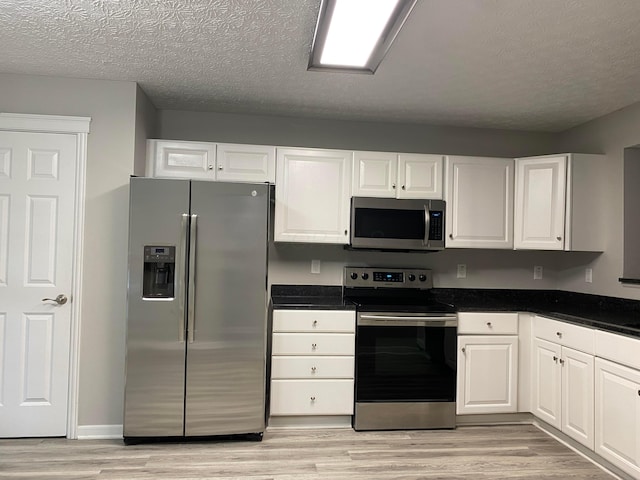 kitchen featuring appliances with stainless steel finishes, dark countertops, white cabinetry, and light wood-style floors