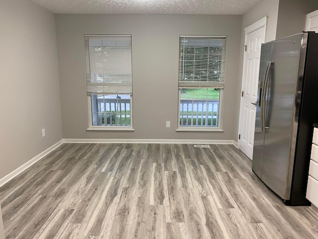 spare room with light wood finished floors, baseboards, and a textured ceiling