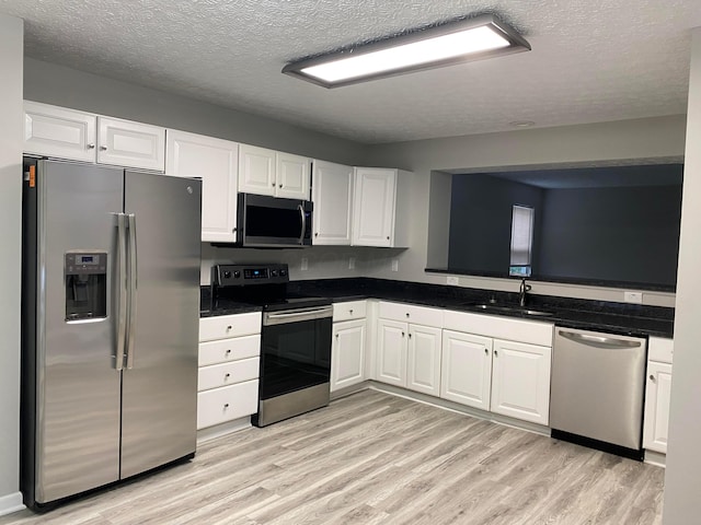 kitchen featuring appliances with stainless steel finishes, white cabinetry, a sink, and light wood finished floors