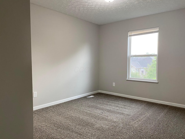 unfurnished room featuring baseboards, visible vents, dark carpet, and a textured ceiling