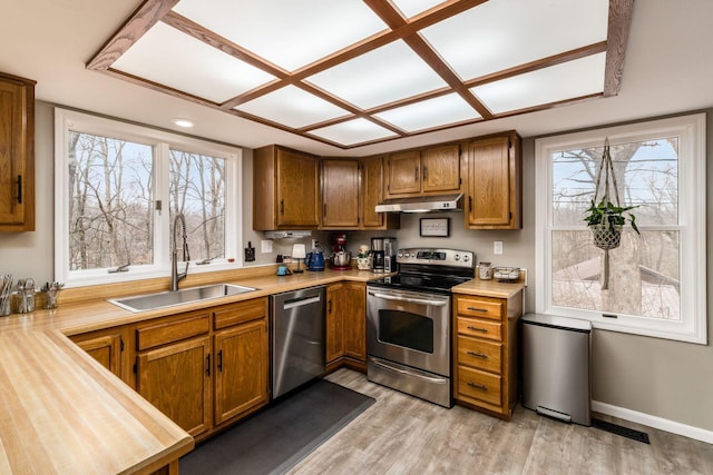 kitchen featuring under cabinet range hood, light countertops, brown cabinets, stainless steel appliances, and a sink