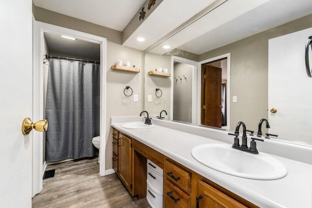 full bathroom with a sink, toilet, wood finished floors, and double vanity