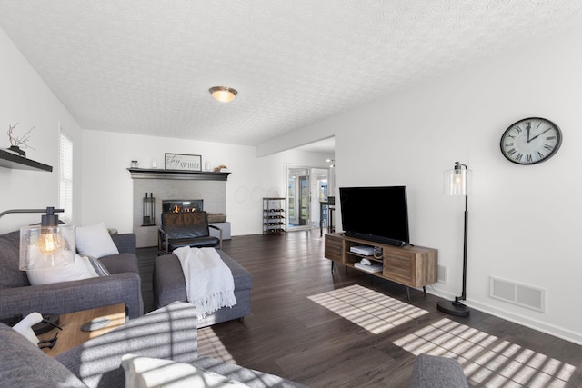 living area with a textured ceiling, wood finished floors, visible vents, baseboards, and a brick fireplace