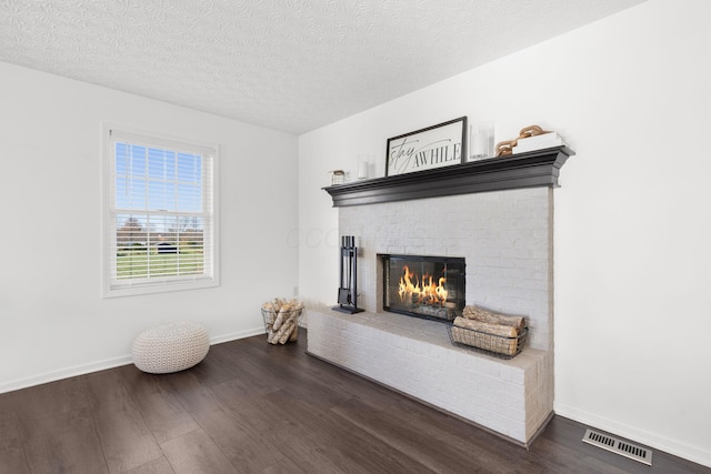 interior details featuring baseboards, visible vents, wood finished floors, a textured ceiling, and a brick fireplace