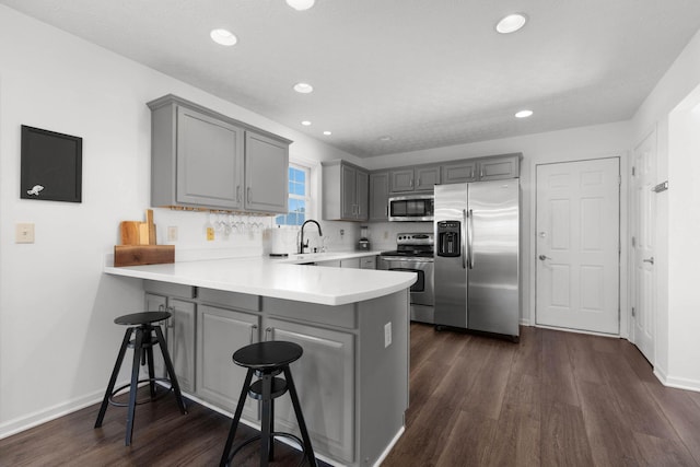 kitchen featuring appliances with stainless steel finishes, dark wood-style flooring, a peninsula, light countertops, and gray cabinetry