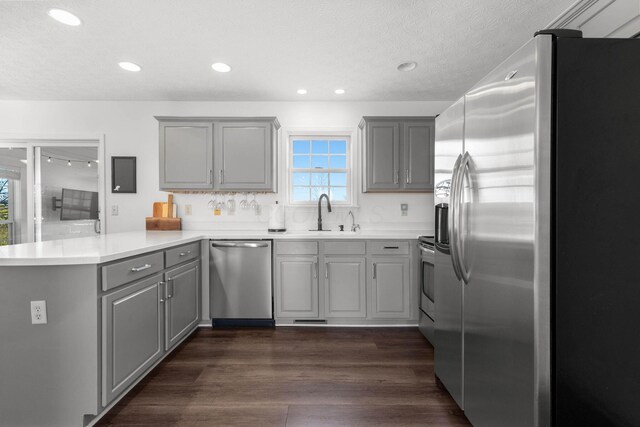 kitchen featuring stainless steel appliances, a sink, a peninsula, and gray cabinetry