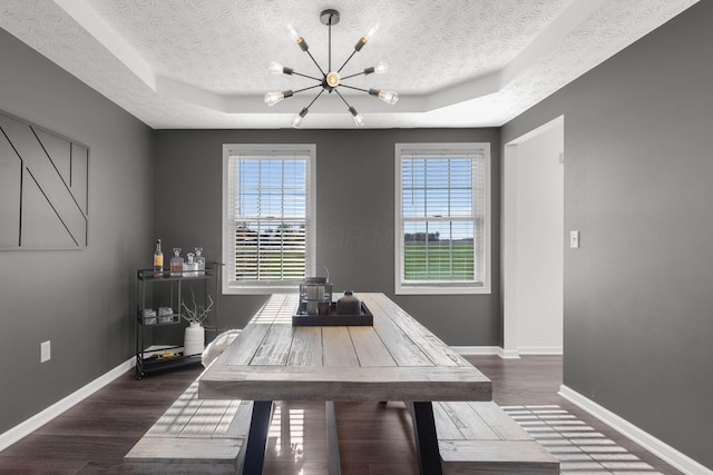 dining area featuring a chandelier, a textured ceiling, dark wood-style flooring, baseboards, and a raised ceiling