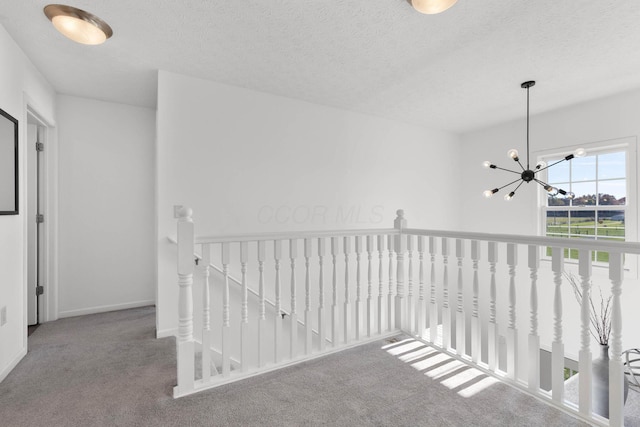 hall featuring a textured ceiling, carpet flooring, and an upstairs landing