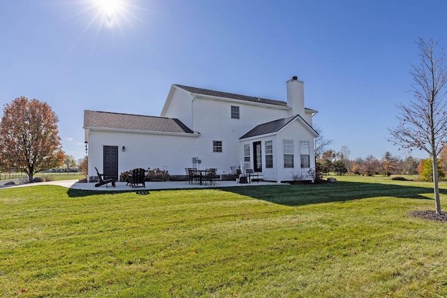 back of house featuring a chimney, a lawn, and a patio area