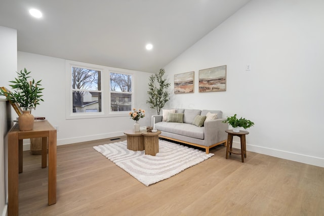 living area featuring lofted ceiling, visible vents, baseboards, and wood finished floors