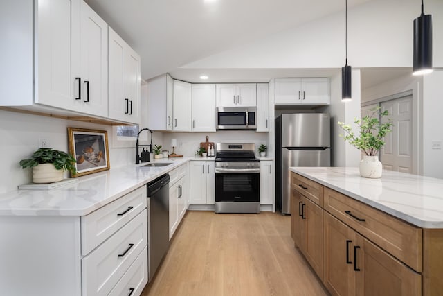 kitchen with light wood-style flooring, appliances with stainless steel finishes, vaulted ceiling, a sink, and light stone countertops