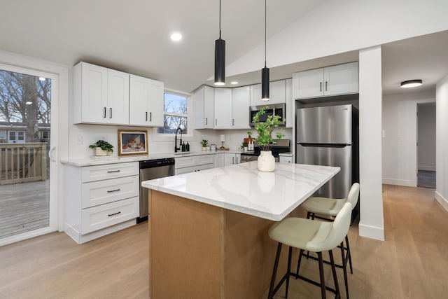 kitchen with a center island, a breakfast bar area, appliances with stainless steel finishes, a sink, and light stone countertops